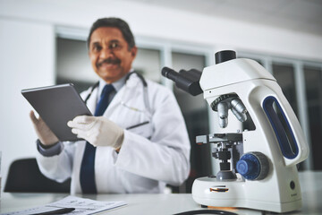 Medical research that makes a difference. Shot of a microscope on a laboratory table with a scientist using a digital tablet in the background.