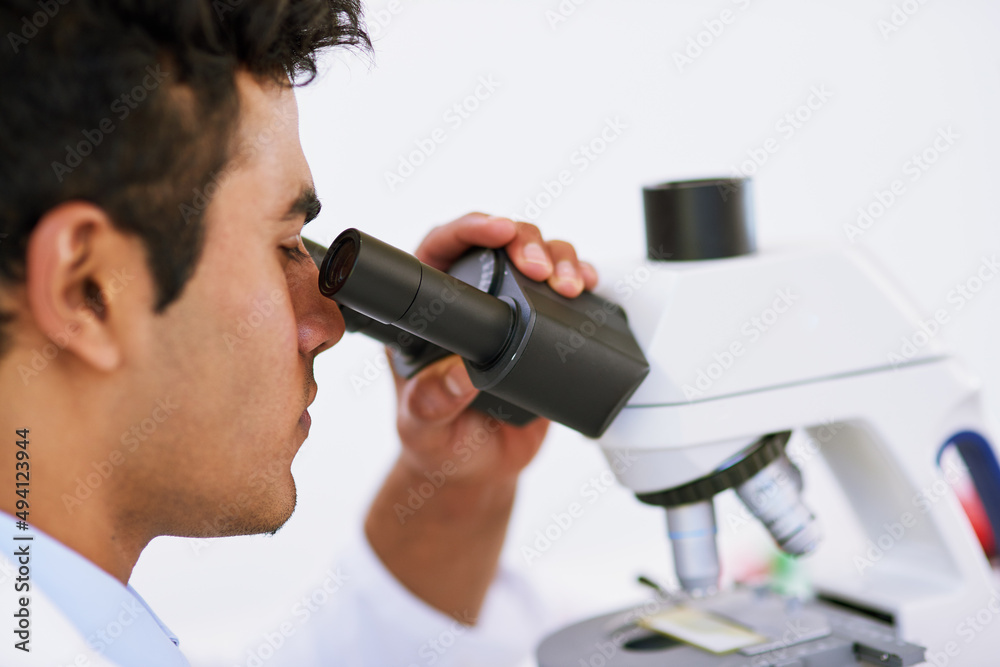 Poster Looking for solutions in the microscopic world. Shot of a lab technician using a microscope while sitting in a lab.