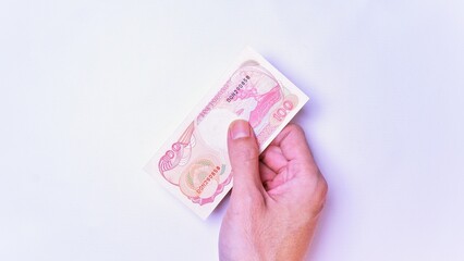 Indonesian Rupiah the official currency of Indonesia. Man's hand is making a payment. Male hand showing Indonesian Rupiah Note. Business Investment Economy and Finance Concept Uang 100 Rupiah IDR