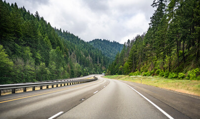 Fototapeta premium Winding wide highway between the green hills overgrown with forests for the free movement of goods and cars between the states