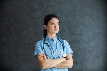 Serious female doctor with stethoscope around neck standing with arms crossed.