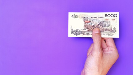 Indonesian Rupiah the official currency of Indonesia. Man's hand is making a payment. Male hand showing Indonesian Rupiah note. Business Investment Economy Money and Finance Concept. Uang 5000 Rupiah