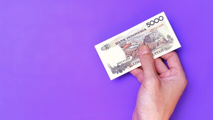 Indonesian Rupiah the official currency of Indonesia. Man's hand is making a payment. Male hand showing Indonesian Rupiah note. Business Investment Economy Money and Finance Concept. Uang 5000 Rupiah