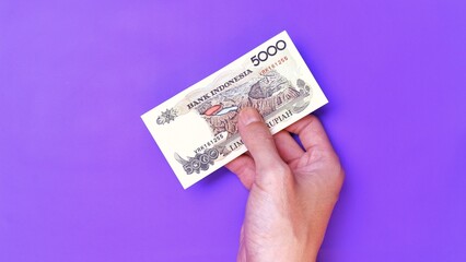 Indonesian Rupiah the official currency of Indonesia. Man's hand is making a payment. Male hand showing Indonesian Rupiah note. Business Investment Economy Money and Finance Concept. Uang 5000 Rupiah