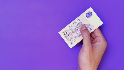 Singapore Dollar is the official currency of Singapore. Business Investment Economy Money Income Loan and Finance concept. Businessman's hand showing Singapore Dollar on a purple background. 2 SGD.