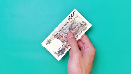 Indonesian Rupiah the official currency of Indonesia. Man's hand is making a payment. Male hand showing Indonesian Rupiah note. Business Investment Economy and Finance concept. Uang 5000 5.000 Rupiah