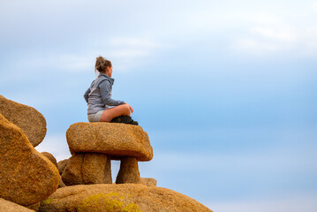 Woman tourist seen in Joshua Tree National Park waiting for sunset views over the desert landscape with bright blue sky background