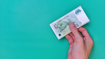 Singapore Dollar is the official currency of Singapore. Business Investment Economy Money Income Loan and Finance concept. Businessman's hand showing Singapore Dollar on a green background. 5 Five SGD