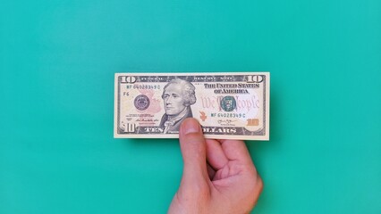 Man's hand is making a payment. Business Investment Economy Money Loan Saving Income and Finance concept. Male hand showing dollar bills on green background. Ten Dollar. 10 USD. Prosperity concept.