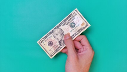 Man's hand is making a payment. Business Investment Economy Money Loan Saving Income and Finance concept. Male hand showing dollar bills on green background. Ten Dollar. 10 USD. Prosperity concept.