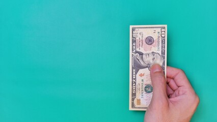 Man's hand is making a payment. Business Investment Economy Money Loan Saving Income and Finance concept. Male hand showing dollar bills on green background. Ten Dollar. 10 USD. Prosperity concept.