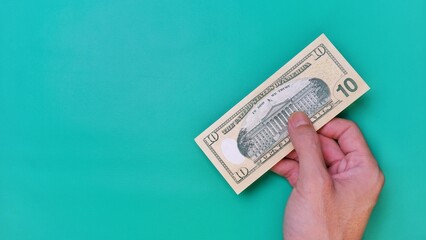 Man's hand is making a payment. Business Investment Economy Money Loan Saving Income and Finance concept. Male hand showing dollar bills on green background. Ten Dollar. 10 USD. Prosperity concept.
