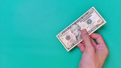 Man's hand is making a payment. Business Investment Economy Money Loan Saving Income and Finance concept. Male hand showing dollar bills on green background. Ten Dollar. 10 USD. Prosperity concept.