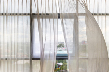 Curtains flutter in the wind from an open window in a wall of square windows