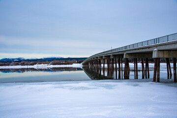 Winter time in northern Canada landscape over the Tagish River with cloudy sky above long bridge. 
