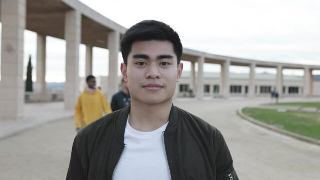 Front view of young confident asian man looking at camera while walking outdoors with group of friends on the background - High quality 4k footage