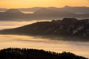Fototapeta premium 霞んだ遠くの山々と朝靄に覆われた湖。日本の北海道の美幌峠から見下ろす屈斜路湖の風景。