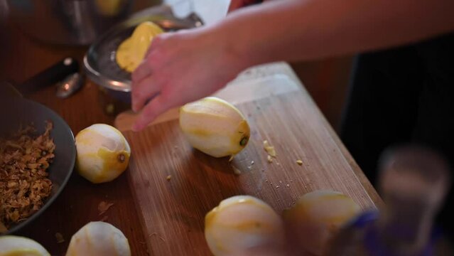 A stationary shot of a woman's hand rolling a peeled lemon against the table and slicing it in half. The counter top is brown and a manual fruit juicer is included on the shot.