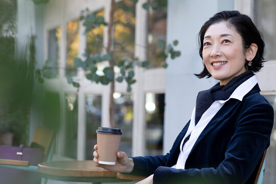 カフェテラスでコーヒーを飲むミドル世代の日本人ビジネスウーマン