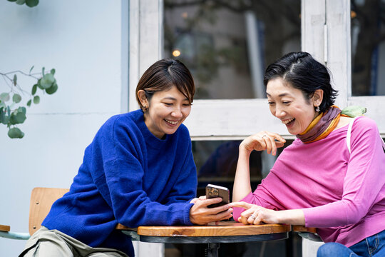 カフェテラスでスマートフォンを見るミドル世代の日本人女性2人