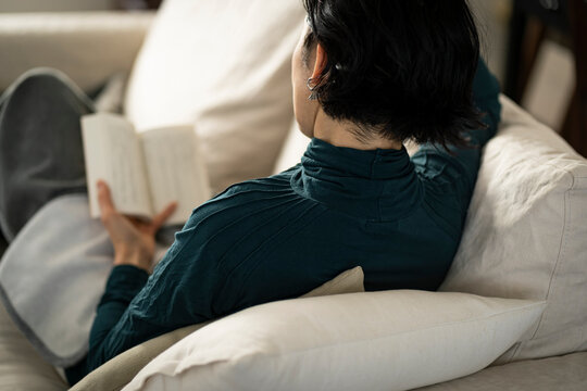 本を読みながらソファでくつろぐミドル世代の日本人女性