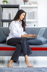 Obraz premium Asian young beautiful happy professional successful female businesswoman in casual outfit sitting on sofa smiling remotely working online during quarantine at home via laptop computer in living room