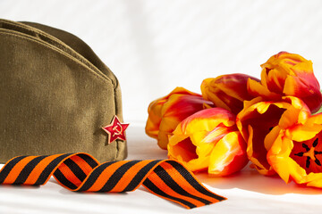 Festive card with tulips, St. George ribbon and military cap on a white background. The concept of the Russian holiday Victory Day, May 9.