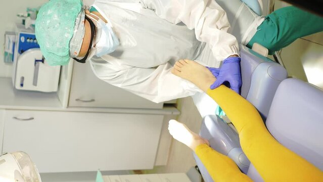 Woman podologist examining patient with chiropody treatment. Vertical video.