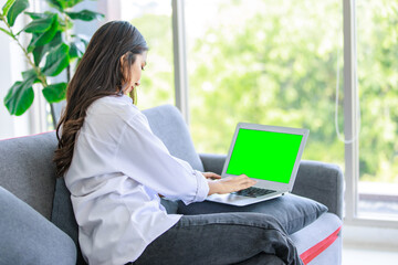 Asian unrecognizable unknown female professional successful businesswoman in casual outfit sitting on cozy sofa typing using green blank screen laptop notebook computer at home office in living room