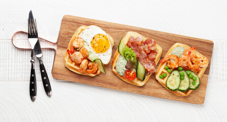 Breakfast waffles with fried eggs, salmon, cucumber and prawns