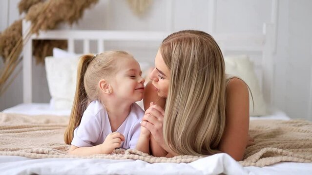mom and daughter play, hug and kiss at home on the bed, lifestyle, tender relationship of a young mother and child, happy family and motherhood