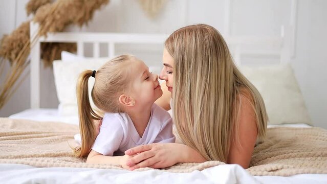 mom and daughter play, hug and kiss at home on the bed, lifestyle, tender relationship of a young mother and child, happy family and motherhood