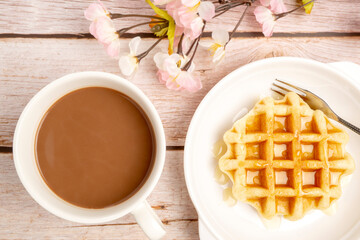 Top View of Freshly Baked Round Butter Waffle, Belgian breakfast pastry dessert, serving with hot cocoa on wooden table.