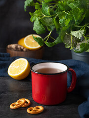 Red  cup of tea with lemon, mint and salt kracker on dark background. The concept of mood breakfast