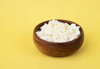 Delicious and nutritious homemade cottage cheese in a wooden bowl on a yellow  background. Concept healthy and diet food. Copy space