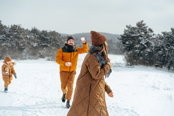 Young family having fun in winter snowy forest