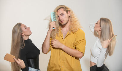 A beautiful young couple of woman with long shiny silky hair and man with blonde curly hair combs hair with comb. Group portrait of young people combing hair.