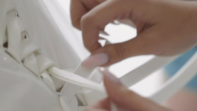 Woman unlaces gorgeous white corset of wedding dress in salon close view. Fashion trends for marriage ceremony. Bride dress and accessories