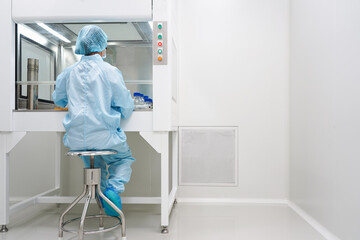 Unidentified microbiologist is testing the sample under the laminar air flow cabinet in the clean room of quality control laboratory in pharmaceutical industry. - obrazy, fototapety, plakaty