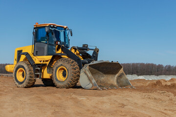 Bulldozer or loader moves the earth at the construction site against the blue sky. An earthmoving machine is leveling the site. Construction heavy equipment for earthworks.