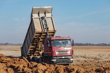 A large mining truck unloads the earth. A soil transporter with a raised body dumps soil.