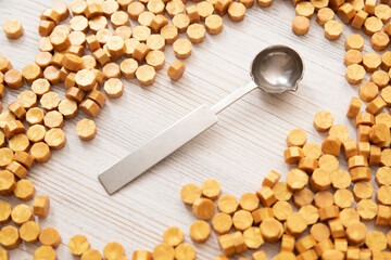 Sealing wax metal spoon and yellow gold sealing wax granules a lot on wooden background, top view.