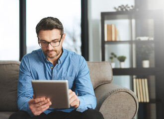 Working on his handheld office. Shot of a businessman using his digital tablet while sitting on a sofa in the office. © Delmaine Donson/peopleimages.com