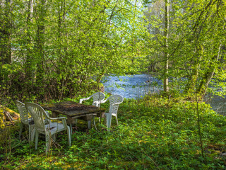 Fototapeta na wymiar Plastic garden furniture in a glade by a river in lush forest