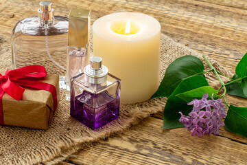 Obraz na płótnie Canvas Bottles of perfume, candle and lilac flowers on wooden background.