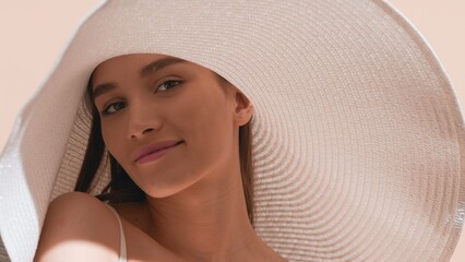 Young gorgeous dark-haired European woman in a big white hat with a smear of sunscreen on her cheek...