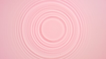 Drop falls down creating circles on water surface on pale pink background | Background shot for beauty commercial
