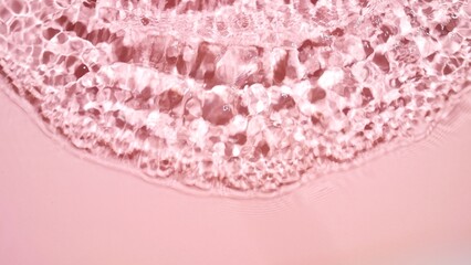 Single wave making ripples and splashes on water surface on pink background | product background, sunscreen commercial