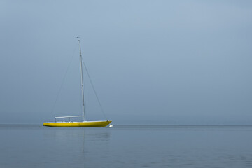 yellow sailboat lying at anchor in the fog