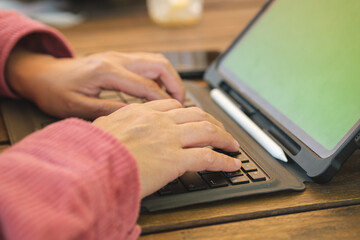 asian woman typing on keyboard with tablet online at coffee shop